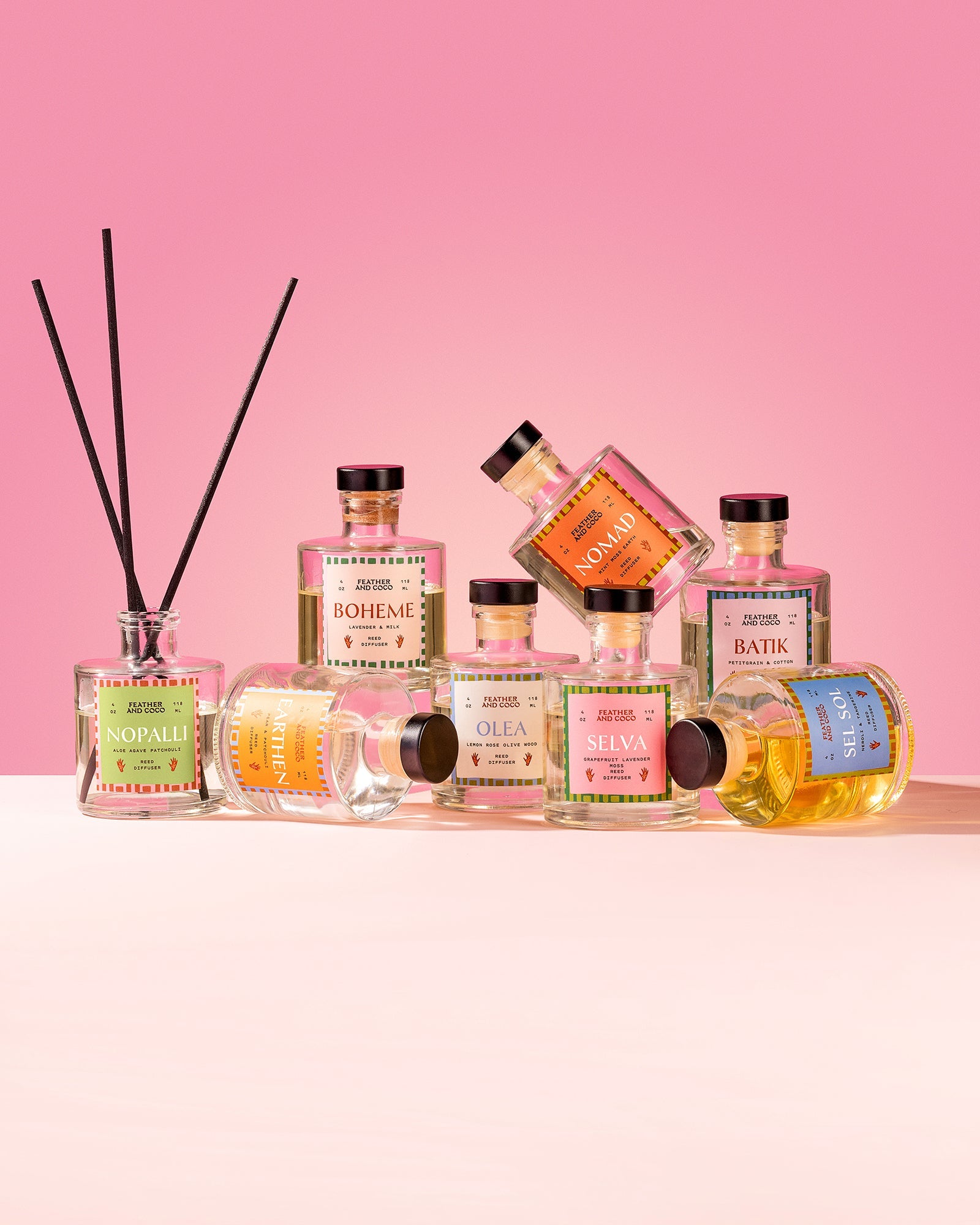 Assorted reed diffusers on a pink background.