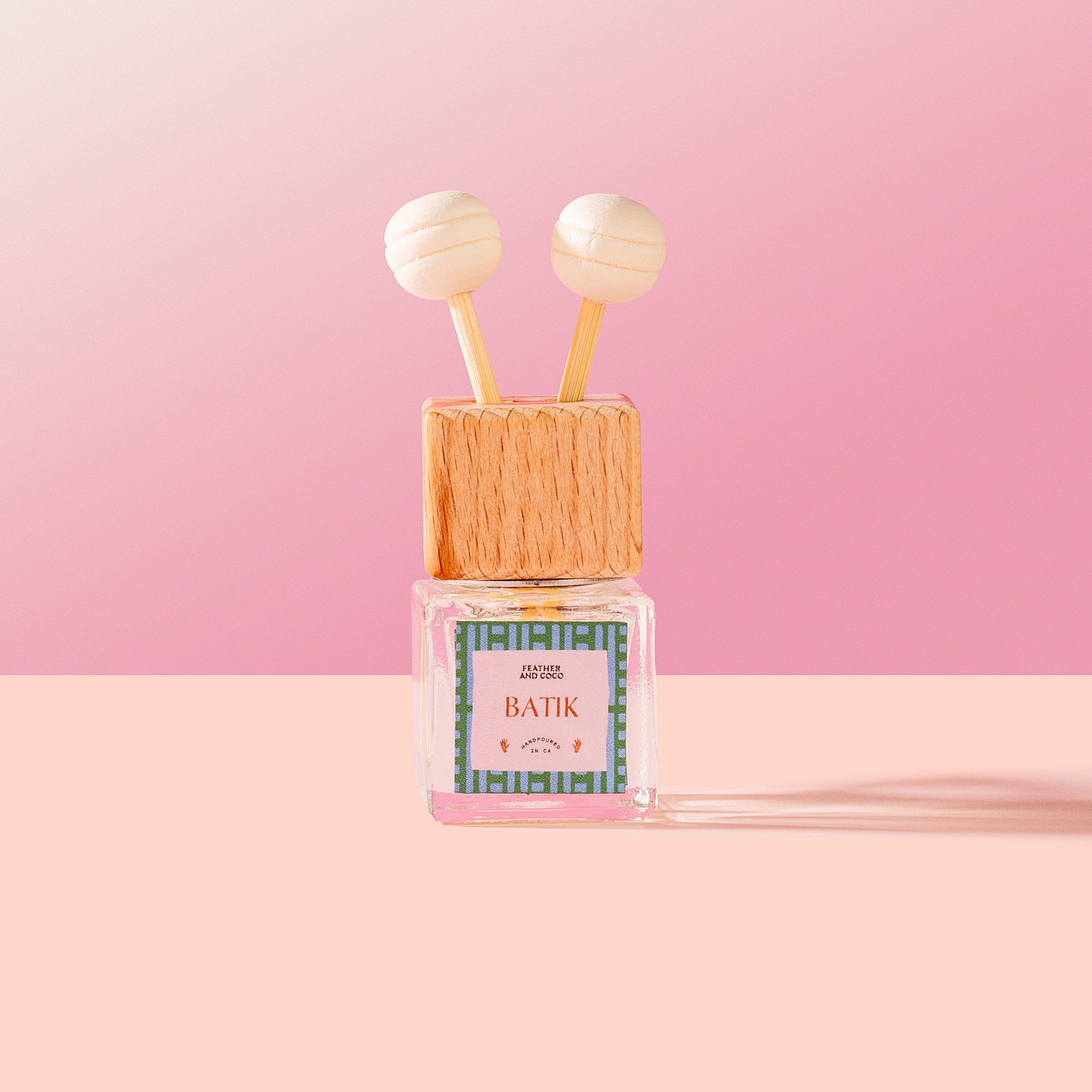 Batik Car Diffuser with wooden cap and pink label on a pink background