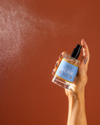 A bottle being sprayed against an orange backdrop. 